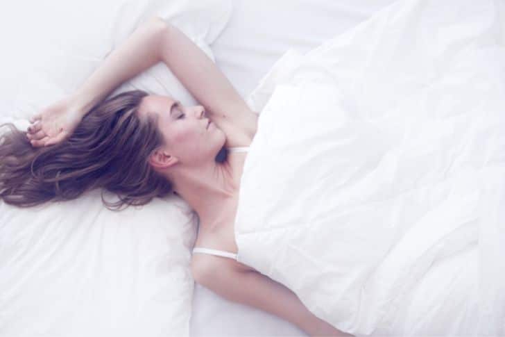 Chica durmiendo plácidamente en una cama con sábanas blancas.