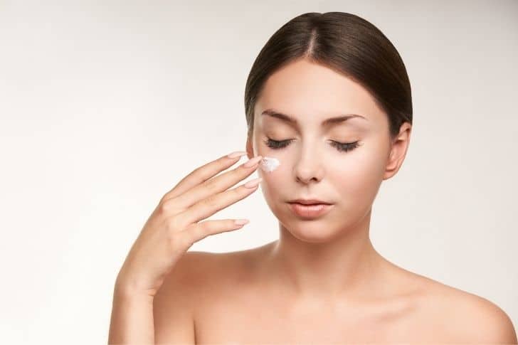 Mujer aplicándose un poco de crema para la piel grasa bajo los ojos.