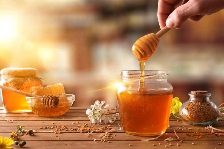 Miel en tarro de cristal con flores sobre mesa de madera.