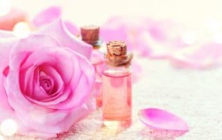 Aceite esencial de rosa de damasco en botellita de cristal junto a flor de rosa de damasco.