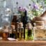Botellas de aceites esenciales de diferentes tamaños sobre mesa de madera y flores naturales al fondo.