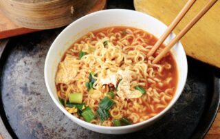 Bol de ramen rápido en 10 minutos con noodles asiáticos, verduras mixtas y otros ingredientes sobre mesa oscura.