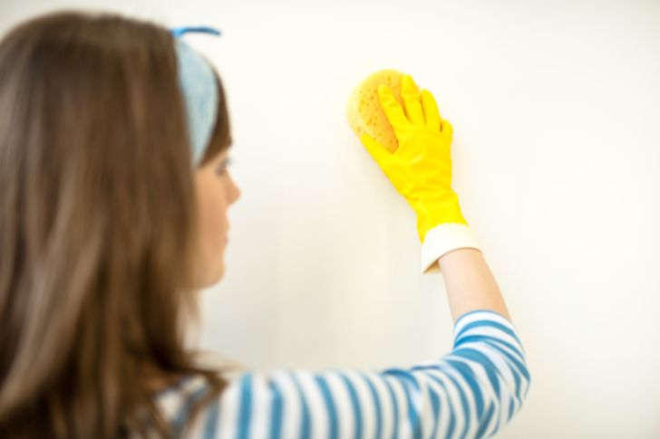 Chica limpiando pared con guantes de limpieza amarillos.